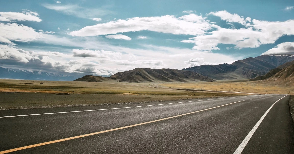 Road crossing an open plain toward distant mountains under scattered clouds.