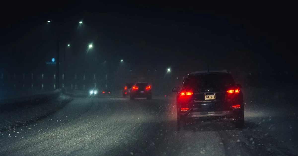 Cars with red taillights driving slowly on a snow-covered road at night in heavy snowfall.