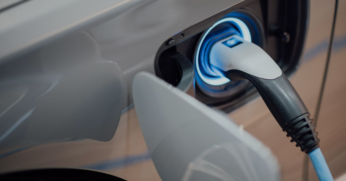 Charging plug connected to an electric car, with a blue light around the charge port.