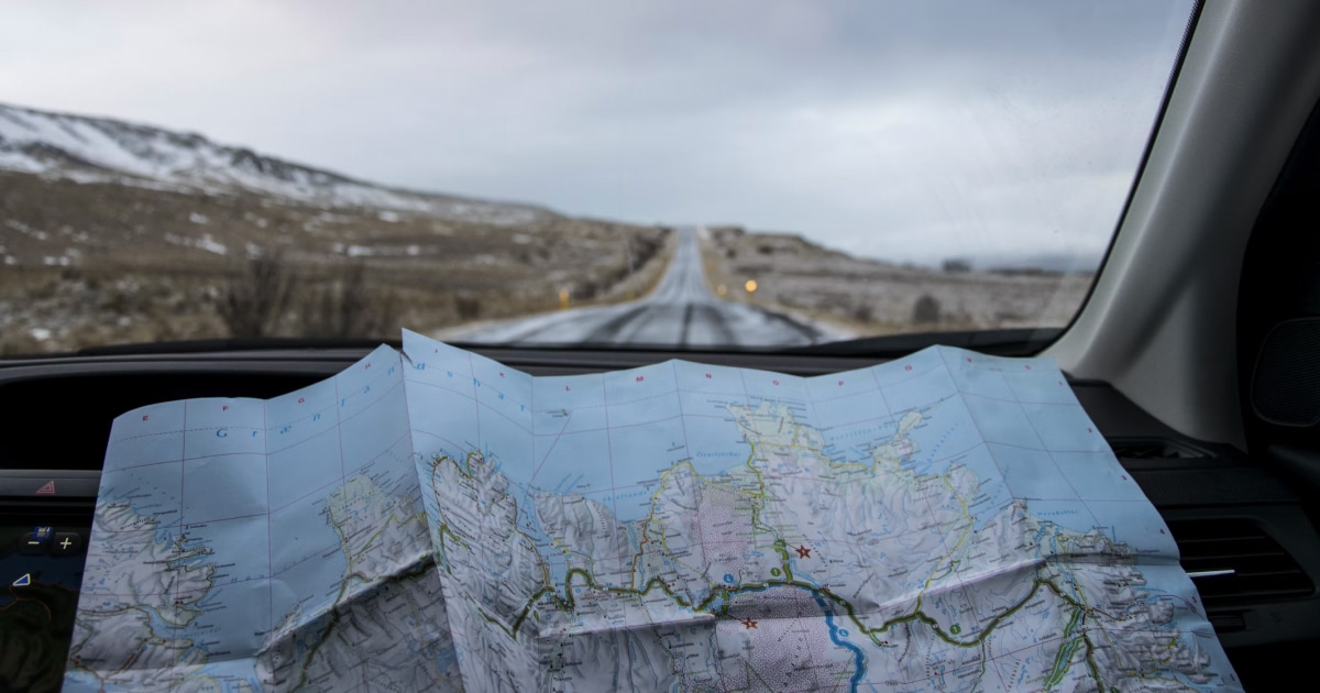 Paper road map open on a car dashboard, with the road ahead visible through the windshield.