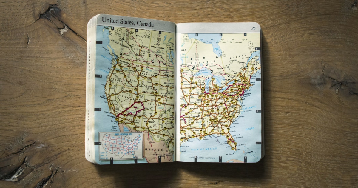 Open road atlas of the United States and Canada on a wooden table.
