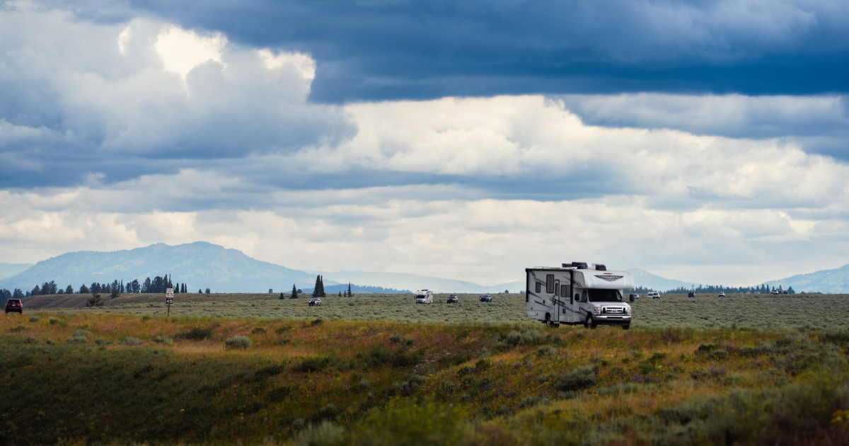 RV parked on a grassy plain with mountains in the distance under scattered clouds.